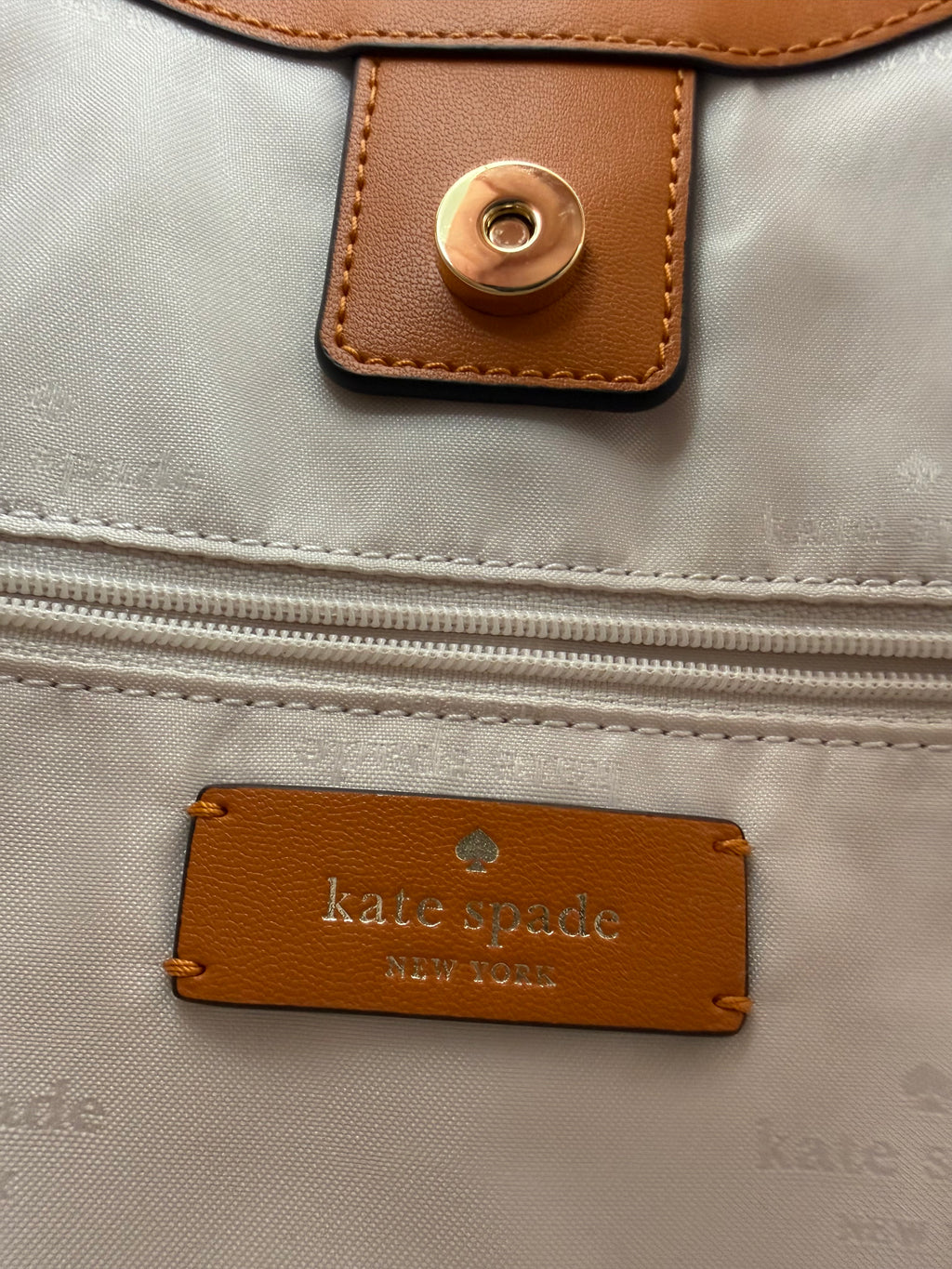 Kate Spade 454 Shoulder  Bag, Farbe Orange Jasper. Hier wird das Logo Patch gezeigt. Das rechteckige Lederstück mit dem eingeprägten Kate Spade New York Schriftstück.