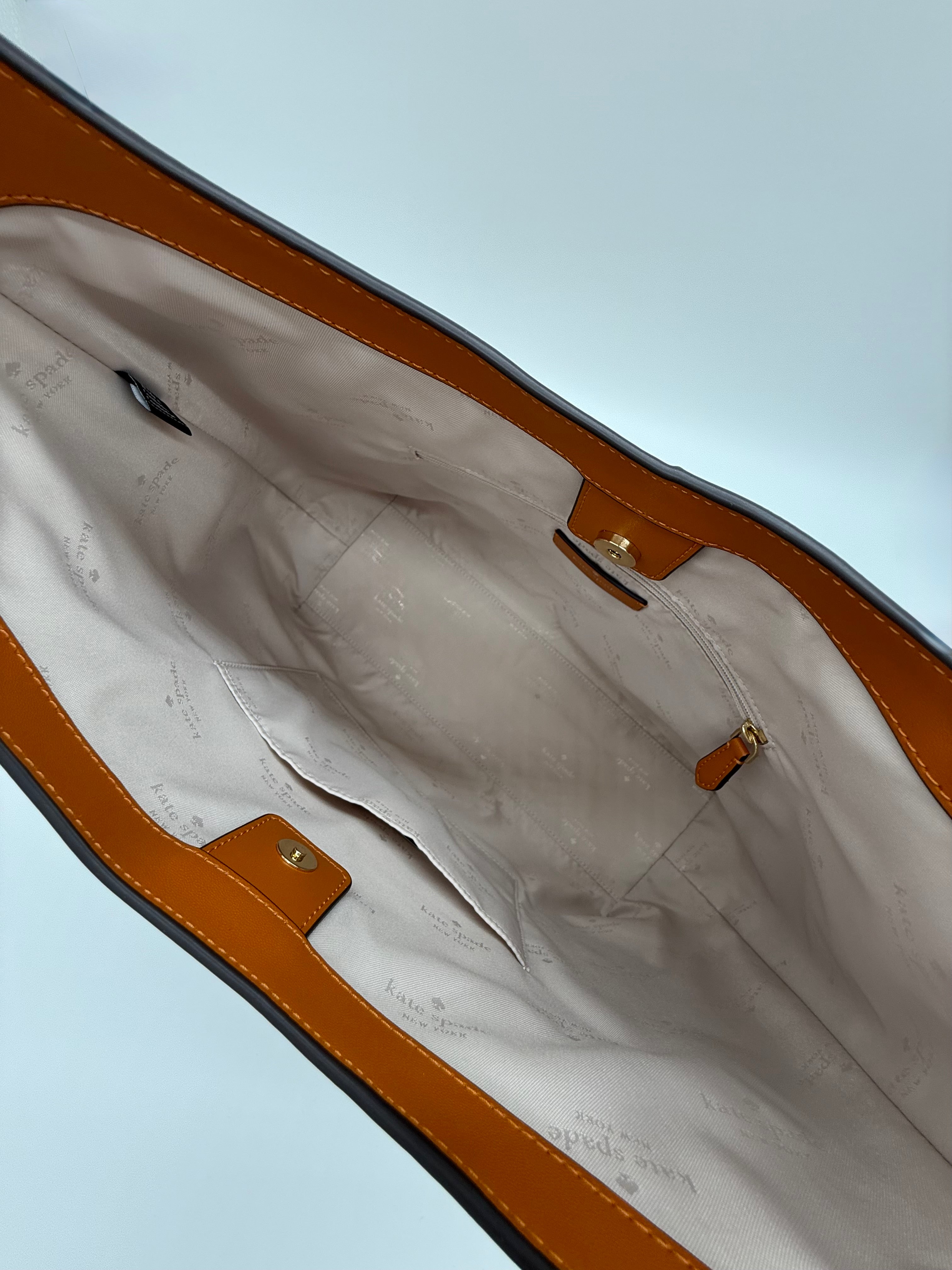 Die Kate Spade 454 Shoulder  Bag, Farbe Orange Jasper Tasche hier sieht man das Signatur-Futter aus hellem Stoff, der mit dem Markenname und Logo gemustert ist. Die Tasche verfügt eine kleine Innentasche und Reissverschlussfach