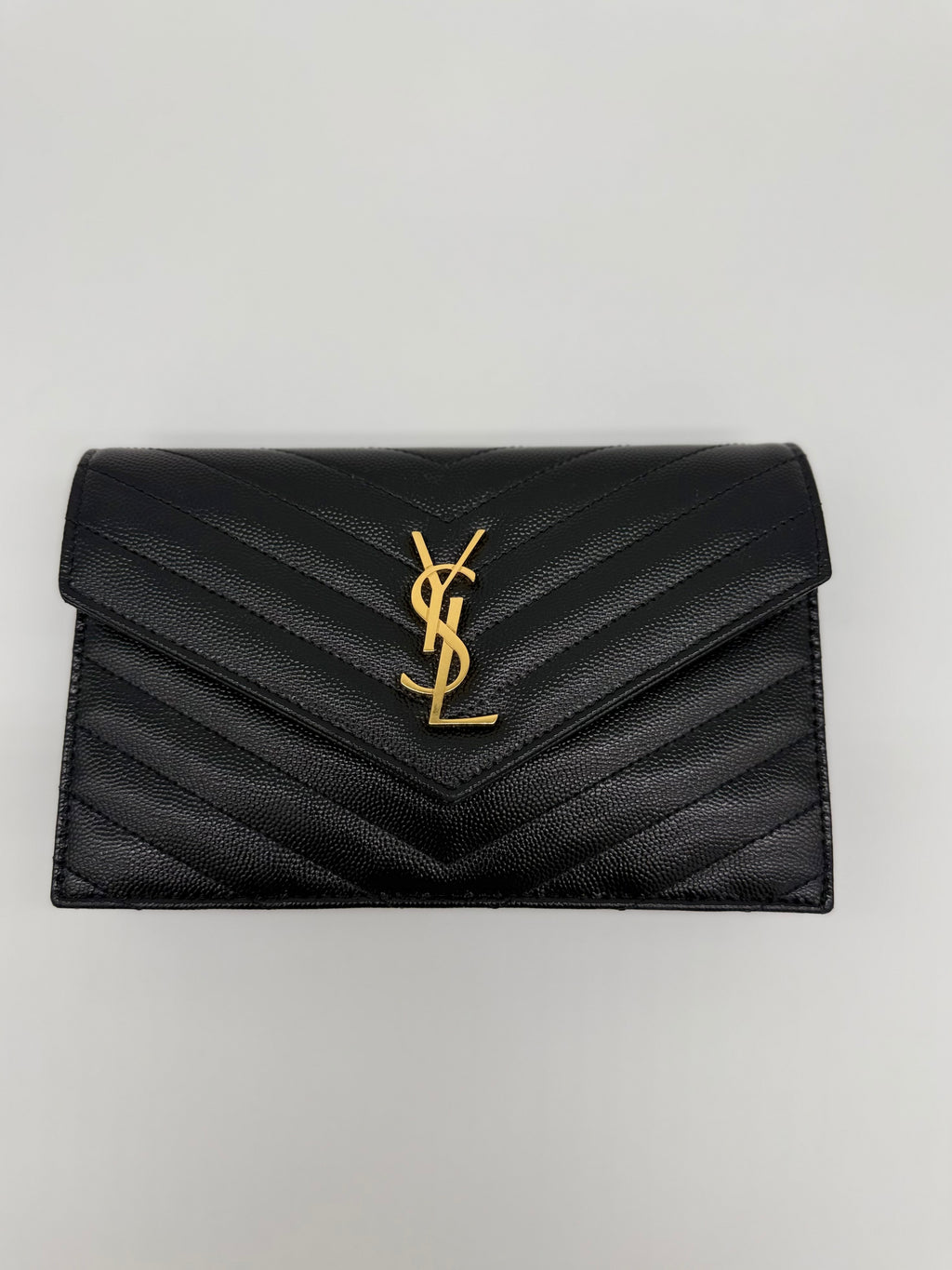 Frontale Nahaufnahme des goldenen YSL Cassandre Logos auf Leder.